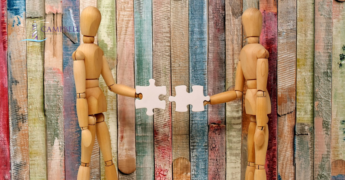 Wooden mannequins holding connecting jigsaw pieces