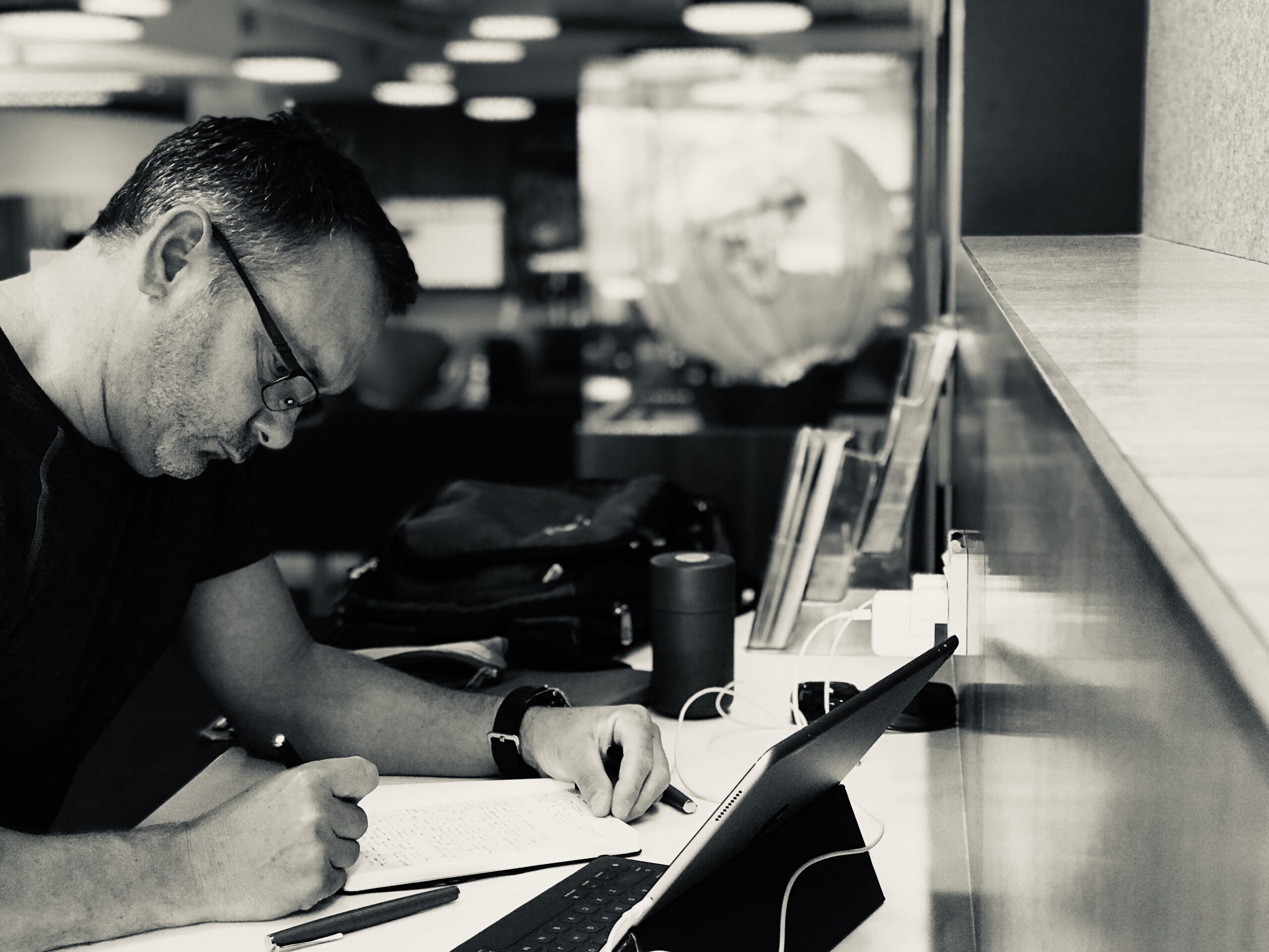 Working man, writing in a notebook with an iPad open in front of him